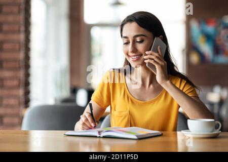 Young lady talking on smartphone while drinking tea at cafe Stock Photo