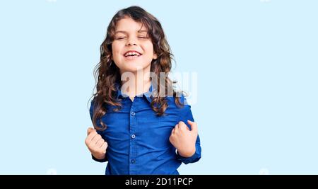 Cute child with long hair wearing casual clothes very happy and excited doing winner gesture with arms raised, smiling and screaming for success. cele Stock Photo