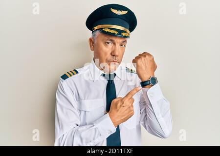 Handsome middle age mature man wearing airplane pilot uniform in hurry pointing to watch time, impatience, looking at the camera with relaxed expressi Stock Photo