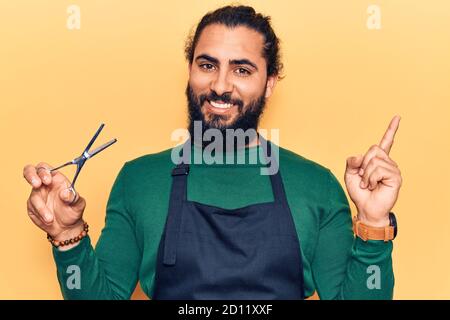 Young arab man wearing barber apron smiling happy pointing with hand and finger to the side Stock Photo