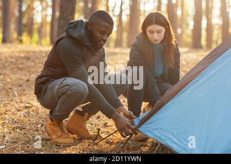 Mixed race couple making tent together, having conversation Stock Photo