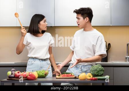 Asian Couple Having Quarrel Cooking Standing In Kitchen At Home
