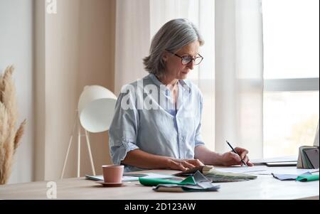 Middle aged stylish woman fashion designer drawing sketches in studio office. Stock Photo