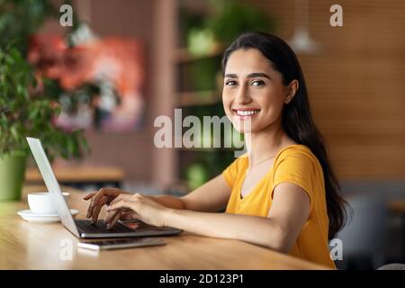 Smiling pretty young woman using laptop at cafe Stock Photo