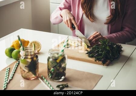 Caucasian woman slicing fruits for making a mojito drink at home using lemons and mint in jar Stock Photo