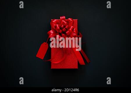 Red christmas box with red bow ribbon and price tag on black background. Black Friday concept. Stock Photo