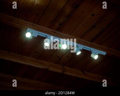 Modern LED Spotlights installed on wooden ceiling. Track lights rotatable lighting downlight glowing in the dark room. Stock Photo