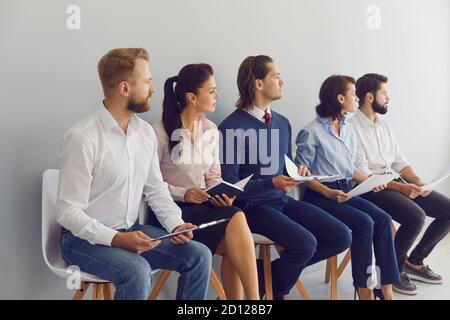 Young candidates sitting in row on chairs waiting for job interview in modern business company Stock Photo