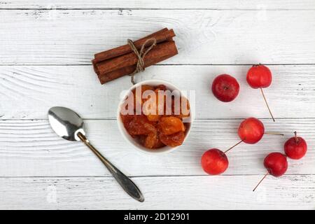 bowl of apple jam, red apples, spoon and cinnamon sticks on white wooden background flat lay. Image contains copy space Stock Photo
