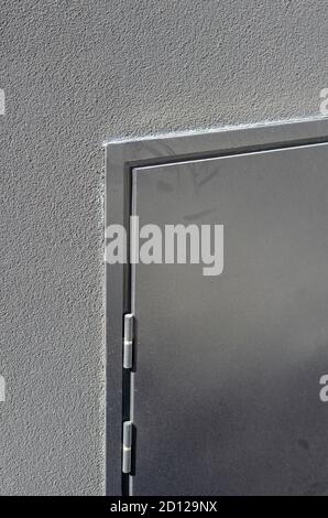 Fragment of a closed metal door in a gray wall. Dusty emergency fire exit door. Geometric Industrial background. Stock Photo