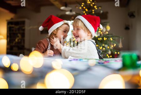 Portrait of small girl and boy indoors at home at Christmas, having fun. Stock Photo