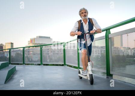 Mature man commuter with electric scooter outdoors in city, going to work. Stock Photo
