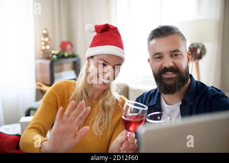 Front view of happy couple indoors at home at Christmas, having video call with family. Stock Photo