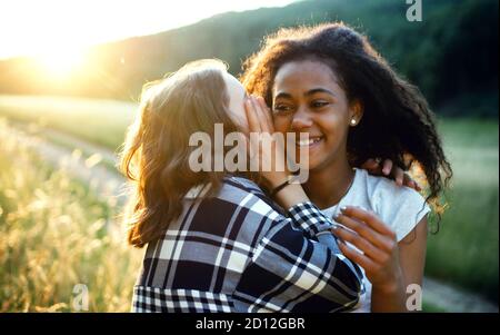 Young teenager girls friends outdoors in nature, whispering in ear. Stock Photo