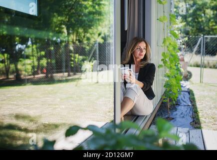 Mature woman working in home office in container house in backyard, resting. Stock Photo