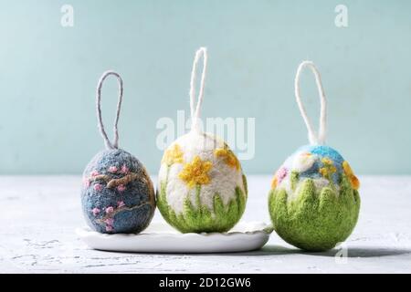 Set of craft felting Easter eggs with blooming flower sakura and green grass decor standing on grey table. Easter decoration and gifts. Copy space Stock Photo