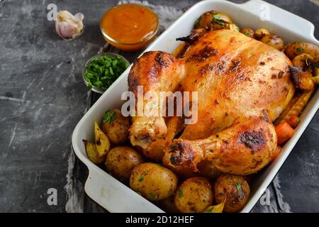 Whole baked chicken. Free space for text. Grey background. Chicken with potatoes, garlic and carrots. Stock Photo