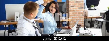 Disabled businessman sits in wheelchair at work table in office and greets businesswoman. Stock Photo