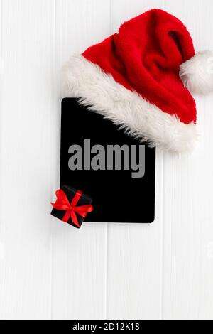 Digital tablet with Santa hat and gift on white wooden background Stock Photo