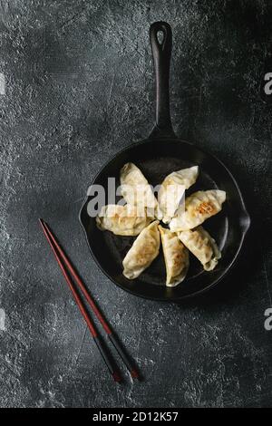 Asian dumplings Gyozas potstickers fried on cast-iron pan, served with chopsticks over black texture background. Top view, space. Stock Photo
