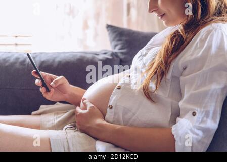 Pregnant woman using cell phone at her home. Stock Photo