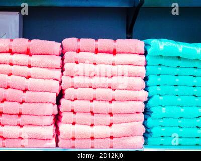 Stacks of pink and turquoise terry towels are stacked on a shelf on a blue background Stock Photo