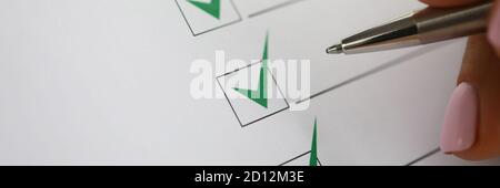 Woman's hand holds pen and marks green check marks in document. Stock Photo