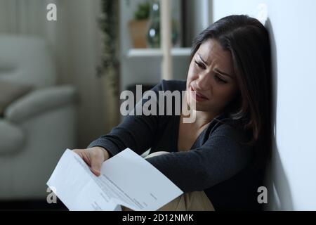 Sad woman complaining after reading a letter sitting on the floor alone at home in the night Stock Photo