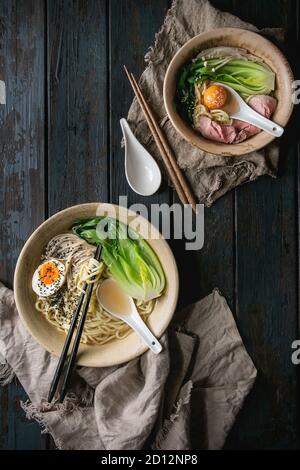 Set of Asian dish udon noodles with boiled egg, sesame, mushrooms, boc choy, sous vide pork meat served in ceramic bowls with spoon and chopsticks on Stock Photo