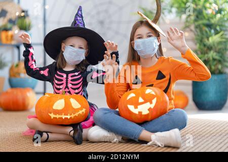 Cute little children girls in carnival costumes wearing face masks. Happy family preparing for Halloween protecting from COVID-19. Stock Photo