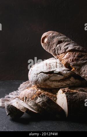 Variety of loafs fresh baked artisan rye and whole grain bread on linen cloth over dark brown texture background. Copy space. Stock Photo