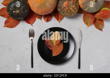Table setting on Thanksgiving Day decorated pumpkin, pears and colorful leaves on grey. Top view Stock Photo