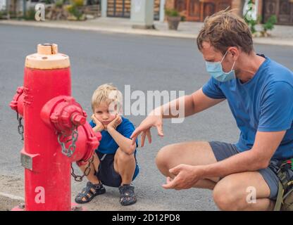 Father influence son worldview family education study everyday knowledge skills. Dad in blue COVID face mask show tell teach child fireman fighters Stock Photo