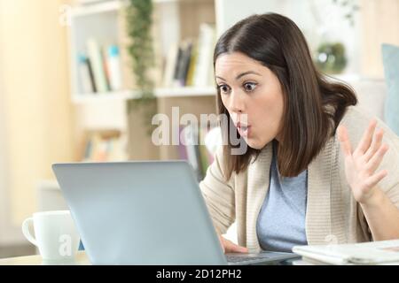 Amazed woman checking good news on laptop sitting on a desk at home Stock Photo