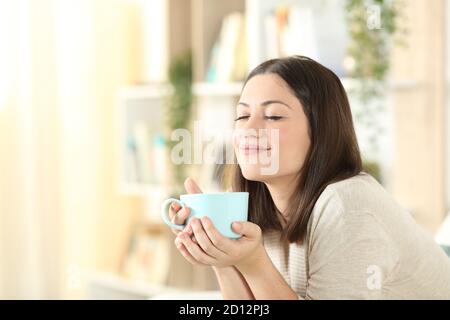 Satisfied woman relaxing holding coffee mug sitting on a couch in the living room at home Stock Photo