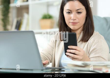 Woman using a laptop and checking a smart phone sitting in the living room at home Stock Photo