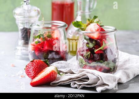 Beetroot and strawberry salad served with arugula and nuts in glass jars with cloth, pepper and bottles of fruit ocet and olive oil over grey table wi Stock Photo