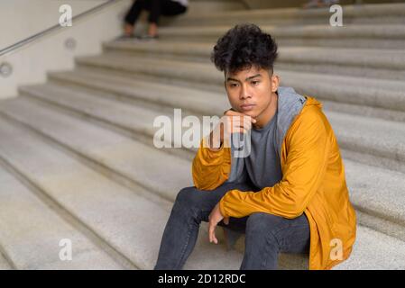 Stressed young Asian man thinking and sitting on staircase in the city