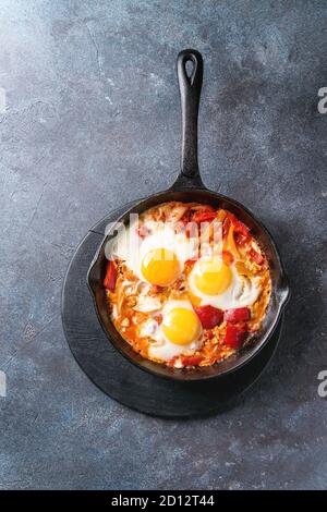 Traditional Israeli Cuisine dishes Shakshuka. Fried egg with vegetables tomatoes and paprika in cast-iron pan on wooden board over blue texture backgr Stock Photo