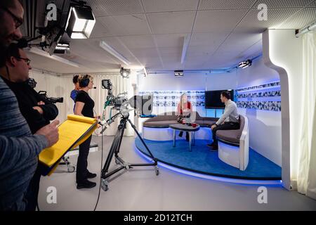 A TV show being filmed in a studio. The presenters are sitting on the studio sofa and talking to each other while the camera crew films them with film Stock Photo