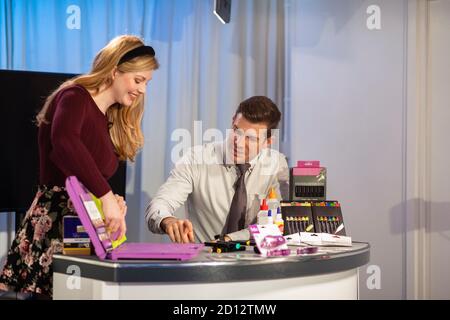 A TV show in the process of being filmed in a studio. The presenters are at the studio desk, selling art supply to the viewers. Stock Photo