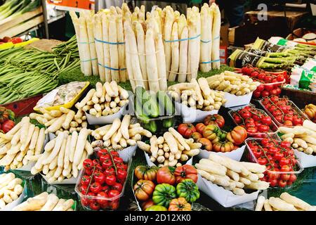 Market stall with fresh spring season vegetables at Parisian street farmers market. White asparagus, tomatoes, cucumbers. Stock Photo
