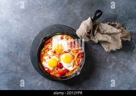 Traditional Israeli Cuisine dishes Shakshuka. Fried egg with vegetables tomatoes and paprika in cast-iron pan on wooden board with cloth over blue tex Stock Photo