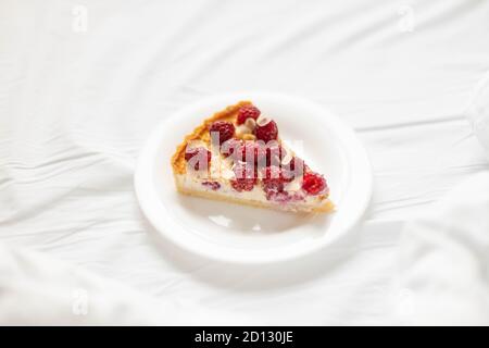 Delicious raspberry piece of cheesecake pie on a white plate on the bed in the room. Stock Photo