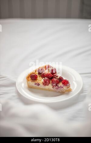 Piece of classic cheesecake with raspberry berries on a white plate on the bed. Vertical orientation Stock Photo