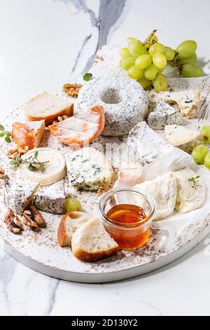Cheese plate assortment of french cheese served with honey, walnuts, bread and grapes on white wooden serving board over white marble texture backgrou Stock Photo