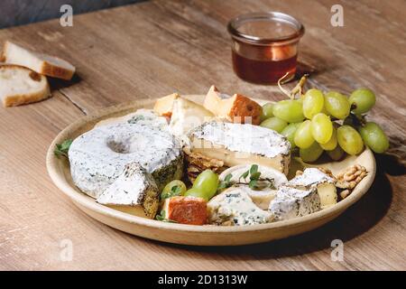 Cheese plate assortment of french cheese served with honey, walnuts, bread and grapes on ceramic plate over wooden table. Close up Stock Photo