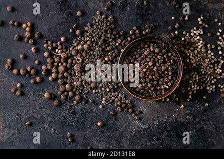 Variety of different black peppers allspice, pimento, monks pepper, peppercorns and ground powder in tin can over old black iron texture background. T Stock Photo