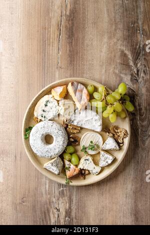 Cheese plate assortment of french cheese served with walnuts and grapes on ceramic plate over wood texture background. Top view, copy space. Stock Photo
