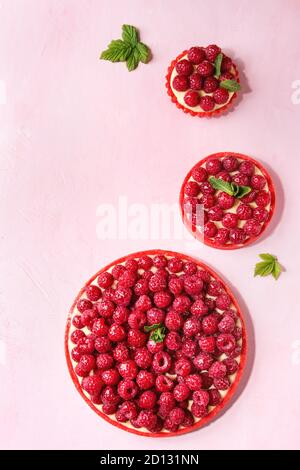 Variety of red raspberry shortbread tarts and tartlets with lemon custard and glazed fresh raspberries over pink pastel background. Top view, space. Stock Photo